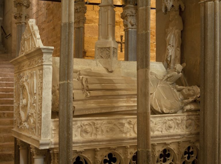Tomba de Jaume II i Blanca de Nàpols Tumba de estilo gótico, con detalles escultóricos en piedra, situada en un recinto iluminado.